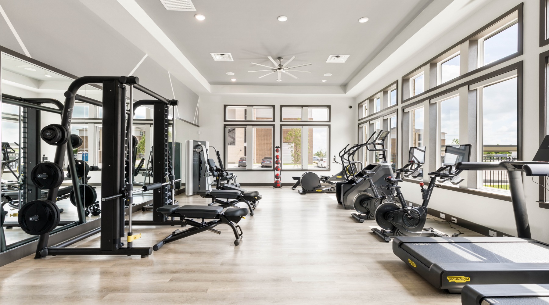 parallax The fitness center at our apartments in Prosper, featuring wood grain floor paneling, treadmills, and other machines.